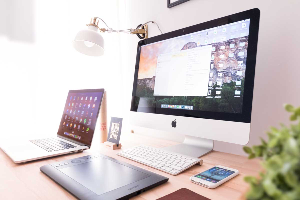 Apple Computer desktop sitting on top of a desk next to a macbook.