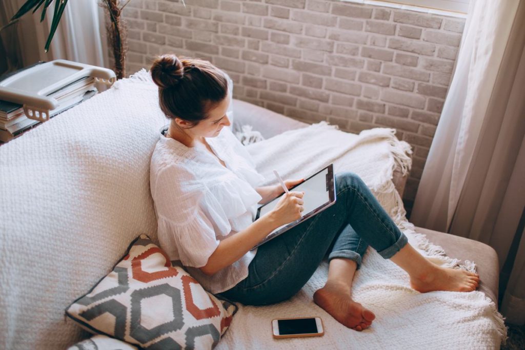 Girl drawing on her ipad while sitting on a couch