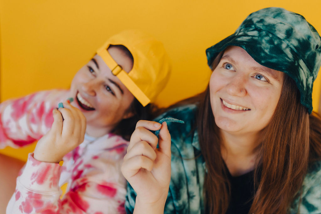 two women in tie dye outfits eating sour candy 