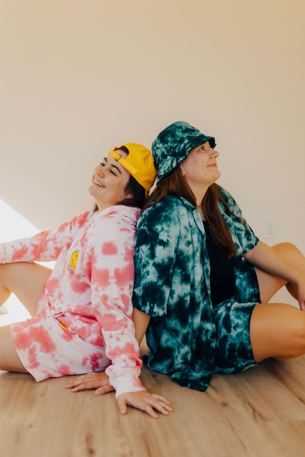 Two girls sit back to back on the floor in tie dye clothing. They are the designers behind the best Showit websites.