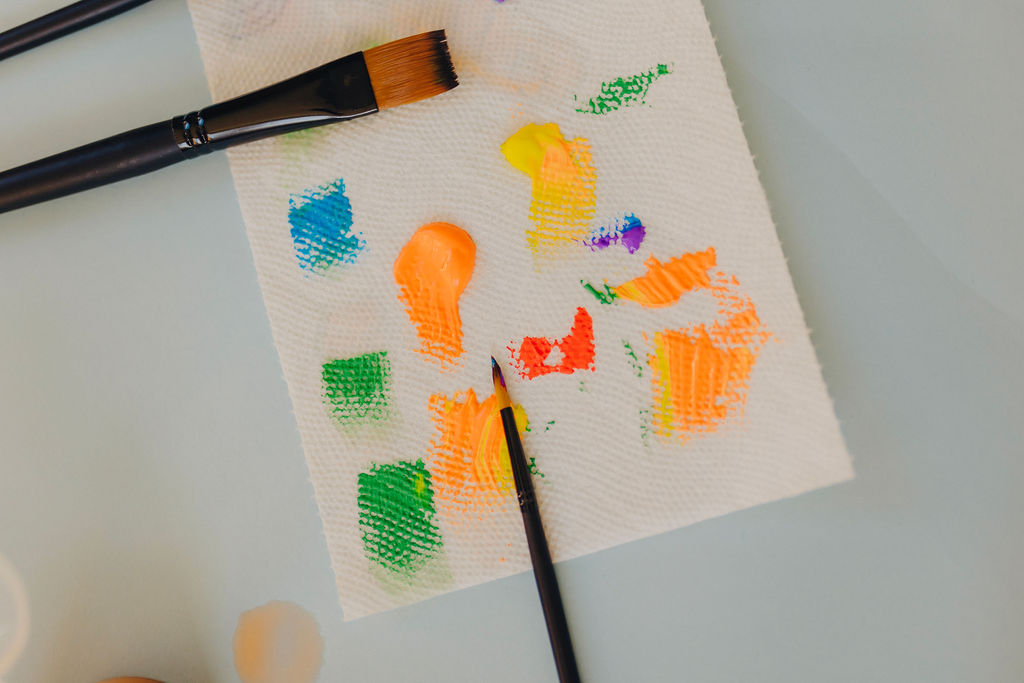 small paint strokes across a paper towel with two paint brushes laying on it 