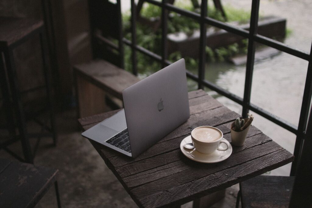 A laptop is on a wooden chair next to a cup of coffee.