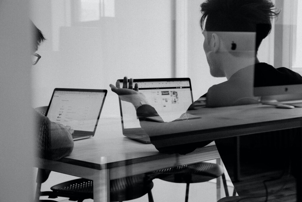 Black and white photo of two people sitting at a table both working on their laptops 