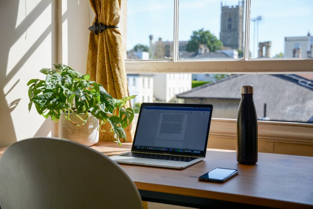 Laptop sitting on a desk next to a water bottle, plant, and cell phone.