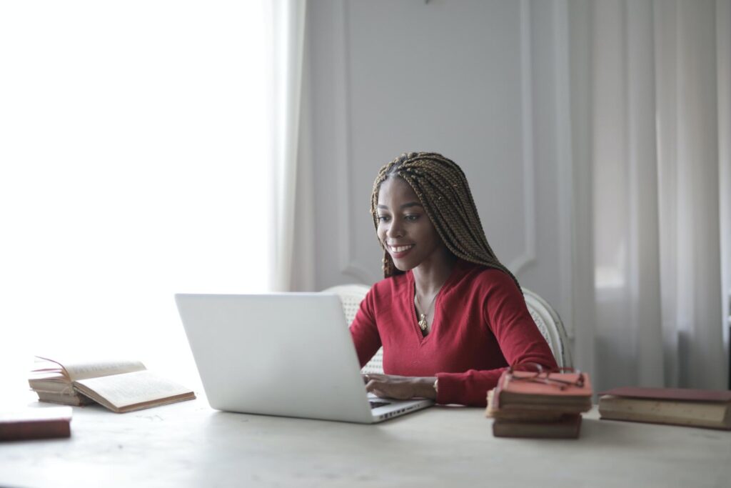 woman sitting at a table working on a laptop with stacks of books on either side of her 