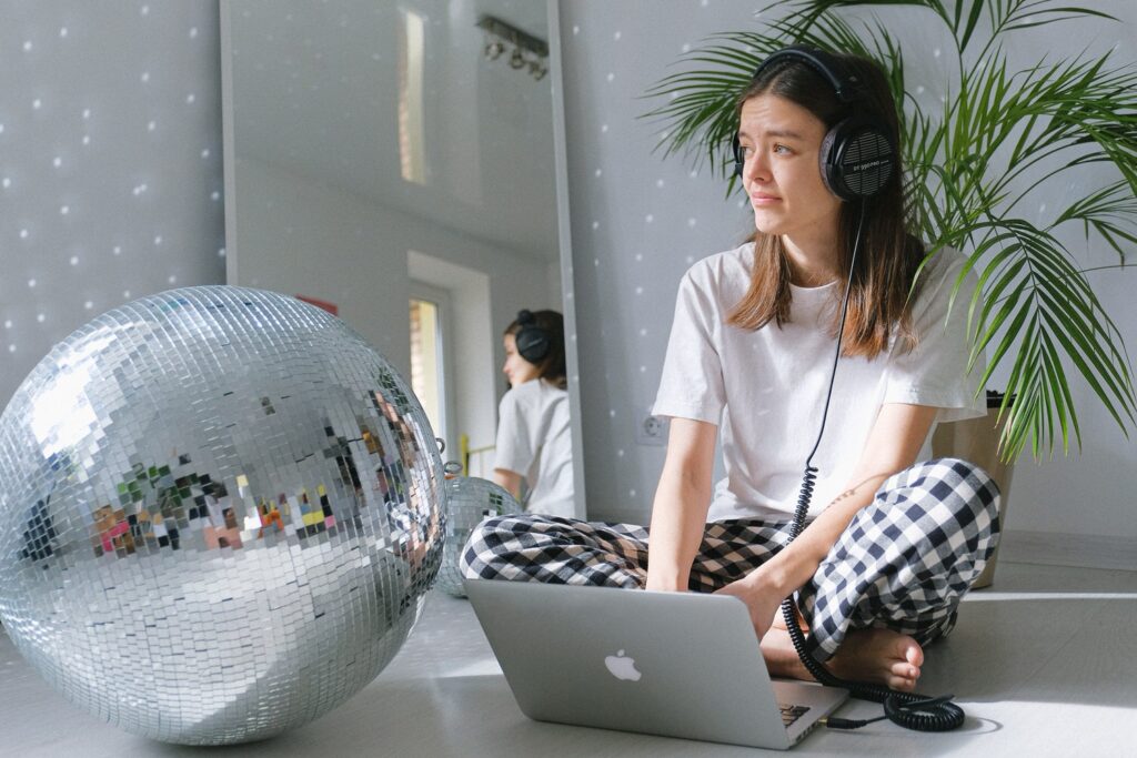 woman sitting on the floor working on a laptop with a disco ball next to her 
