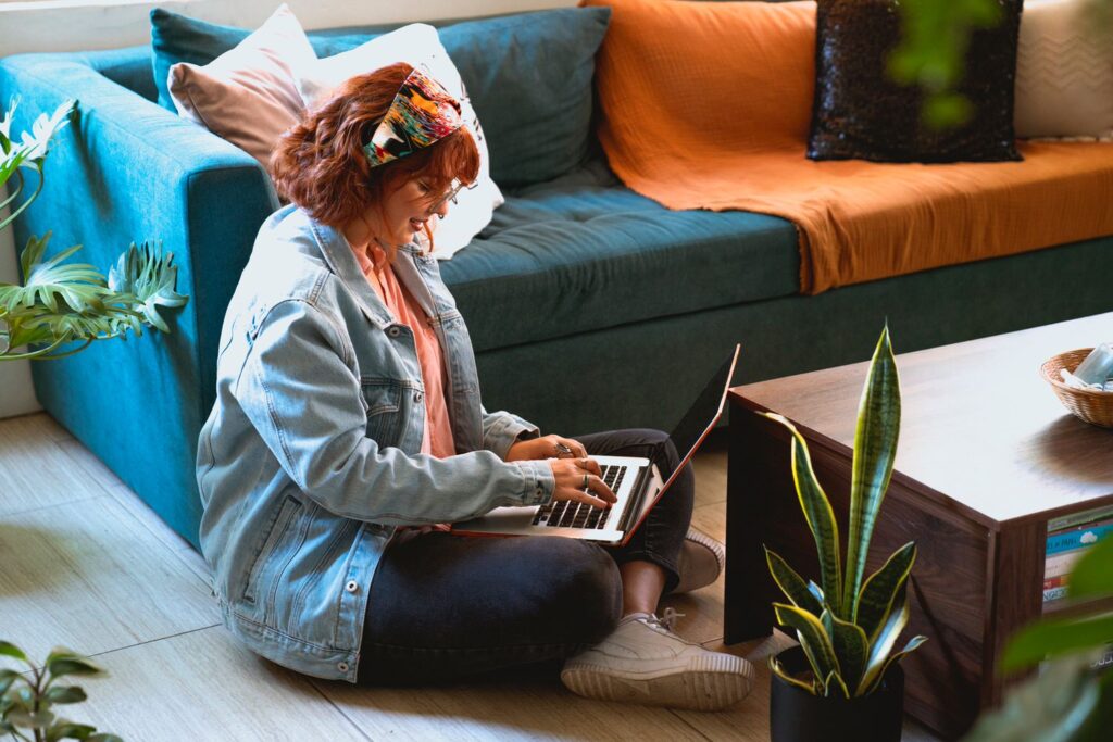 woman sitting on the floor next to her couch typing on a laptop 
