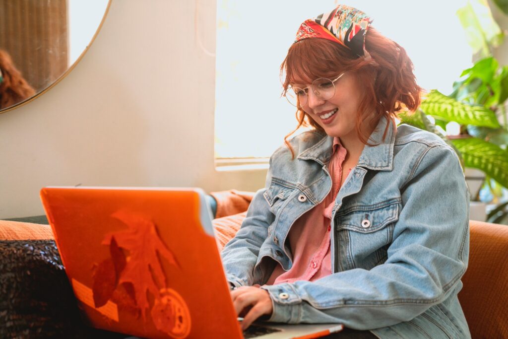 woman smiling as she types on her computer while she is sitting on a couch 