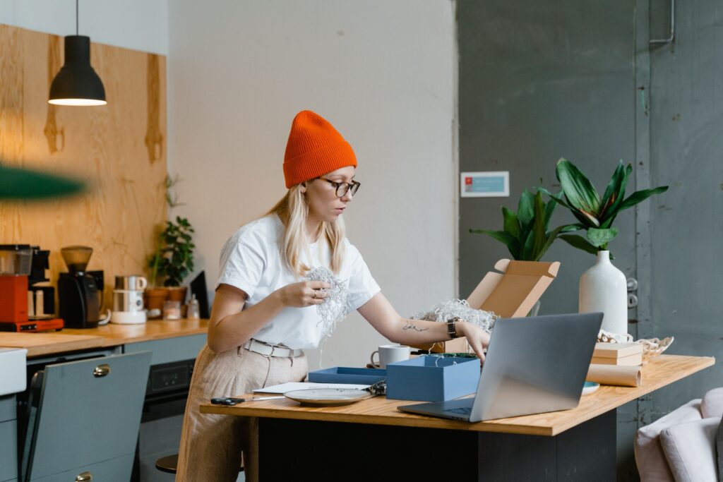 Woman standing at a kitchen island unpacking a box her her laptop open in front of her 