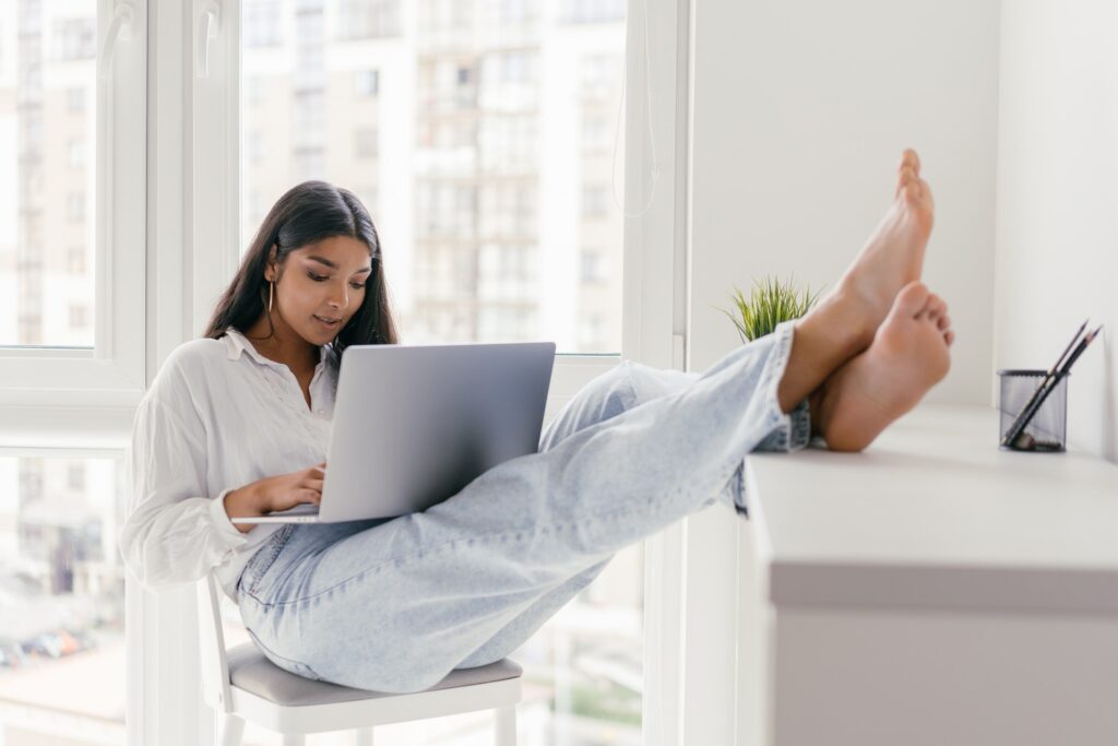 woman with a laptop on her lap and her feet propped up on a small desk 