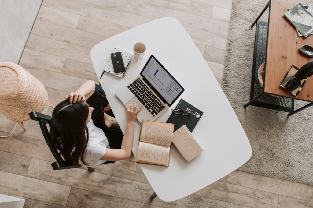 overhead view looking down on someone working on a laptop at a desk with books laid around her 