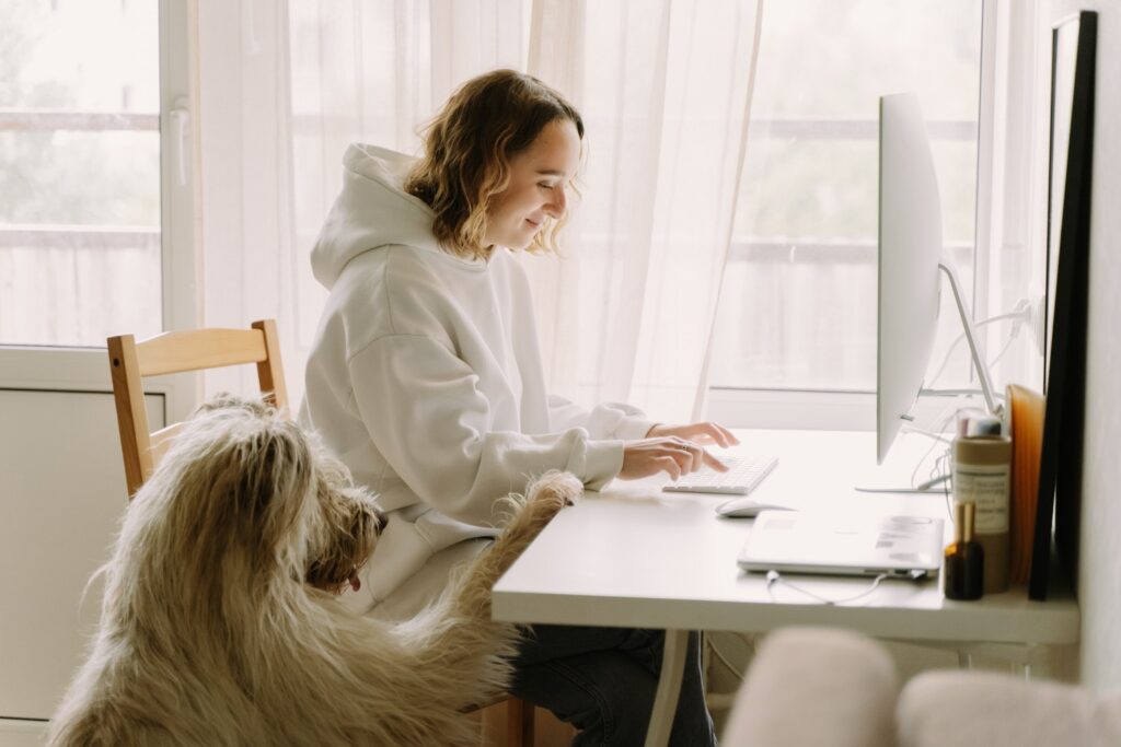 Girl typing on her laptop next to her dog.