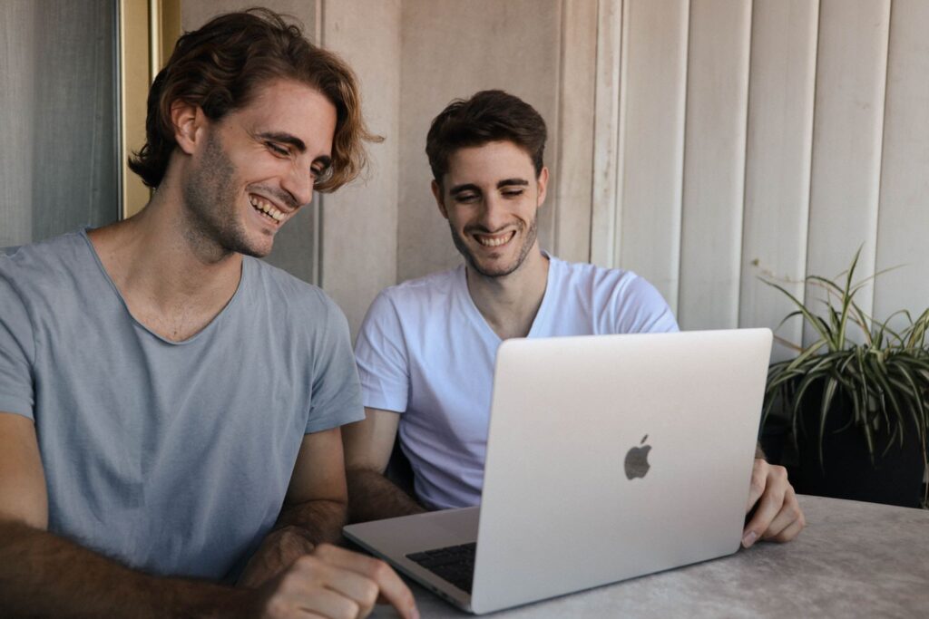 Two men sitting at a small table looking at an open laptop 