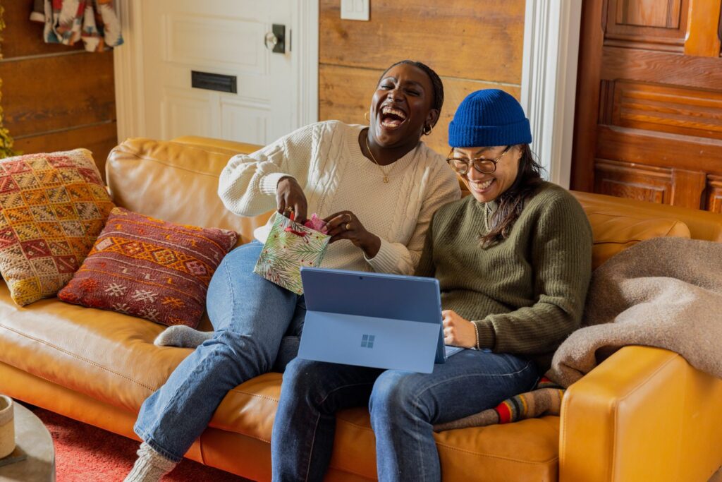 Two people sit on a yellow couch laughing while on a blue laptop.