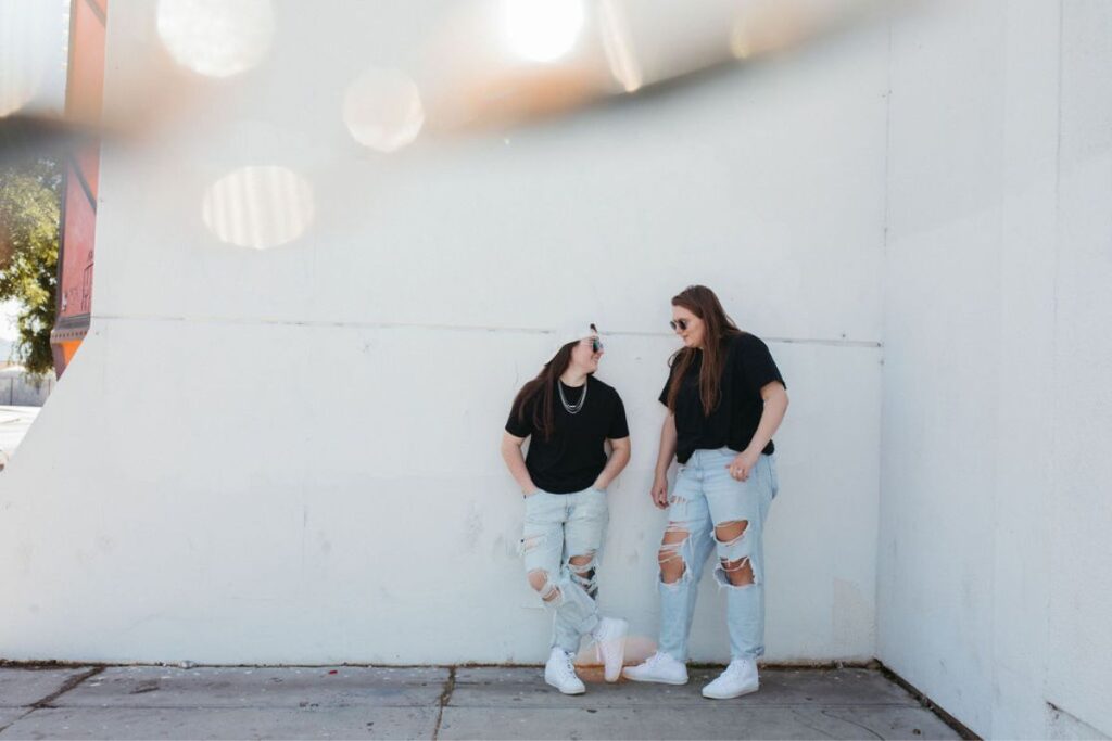 Two girls standing next to a white wall.