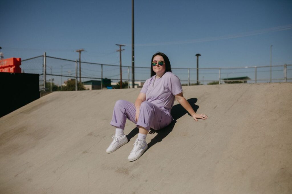 Girl in purple outfit sitting on a skate ramp.
