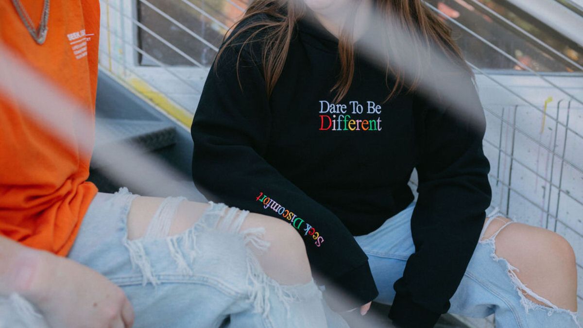Featured image for How often should I blog for SEO. Two women sitting on a staircase with a focus on one of their sweatshirts that reads "Dare to be different".