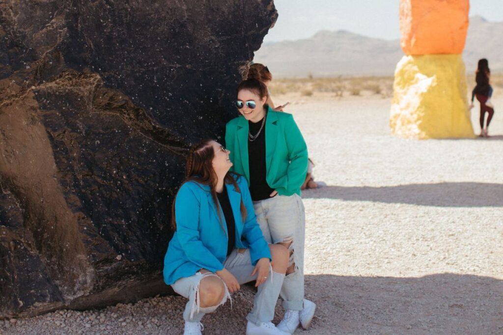 Two girls in blazers crouched down in front of a black rock.