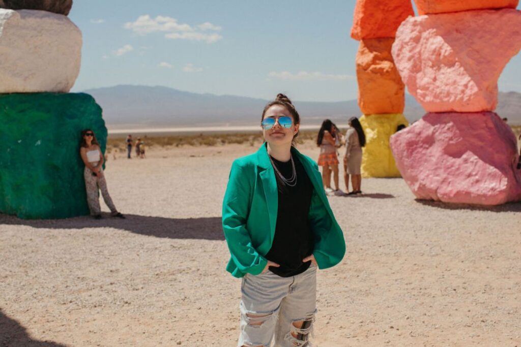 A girl in a green blazer poses in the desert surrounded by colorful rocks.