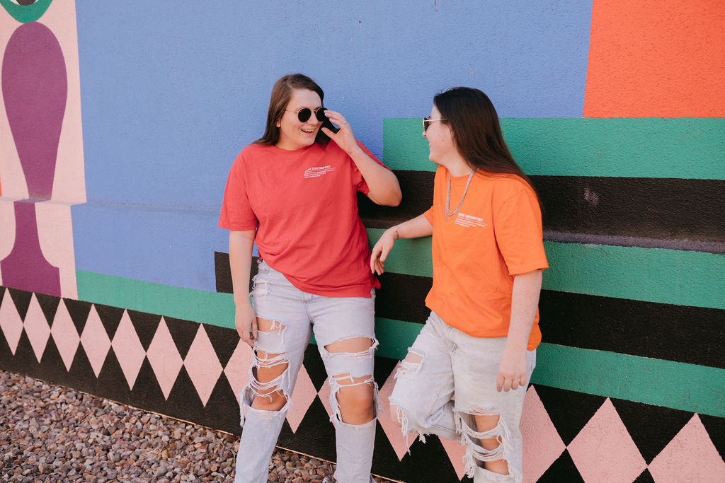 Featured image for why your business needs SEO showing two women leaning up against a colorfully painted wall as they look at each other and smile.