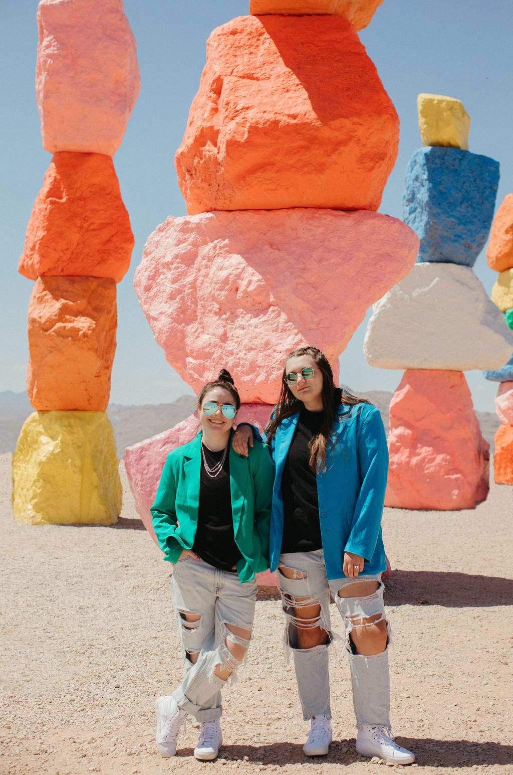 Featured image for photography website tips of two women in bright suit jackets leaning on each other. Behind them are stacks of brightly colored rocks.