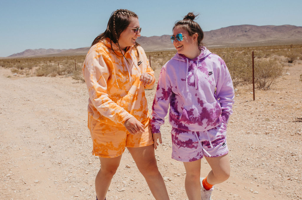 Two women in sweatsuits laughing and walking in a desert together. 