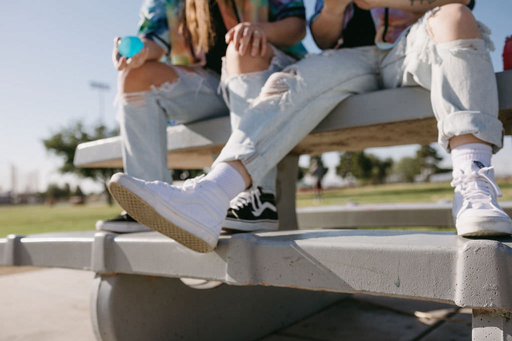 A close up view of a person's leg kicking out while sitting on a picnic table next to another person. 