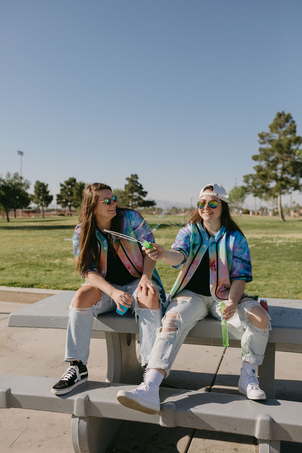 Featured image for passive income ideas for creatives showing two women sitting on a picnic table smiling while one swing a bubble wand in front of them.