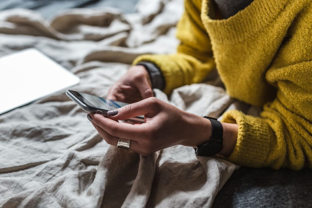 Detailed view of a woman in a yellow sweater browsing on a smartphone, with a smartwatch on her wrist, symbolizing active engagement in digital communication and technology use.