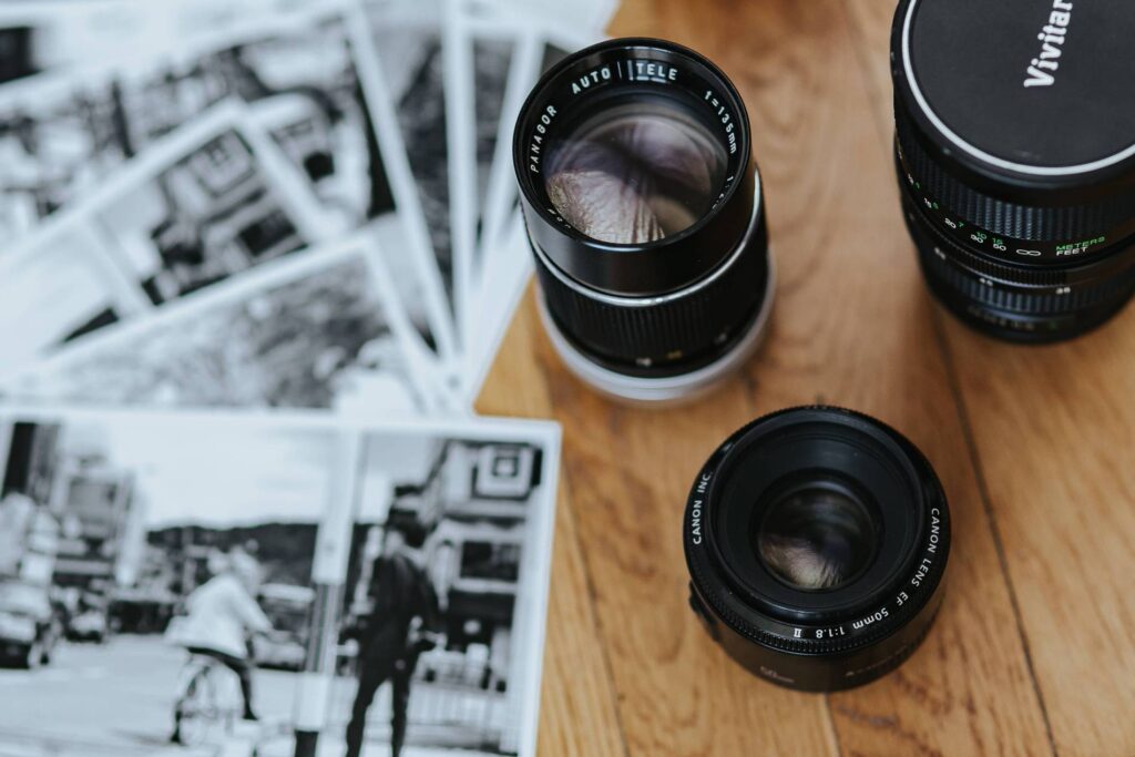 Close-up of two camera lenses with focus on a Vivitar lens, surrounded by black and white street photography prints, showcasing tools of a photography enthusiast.