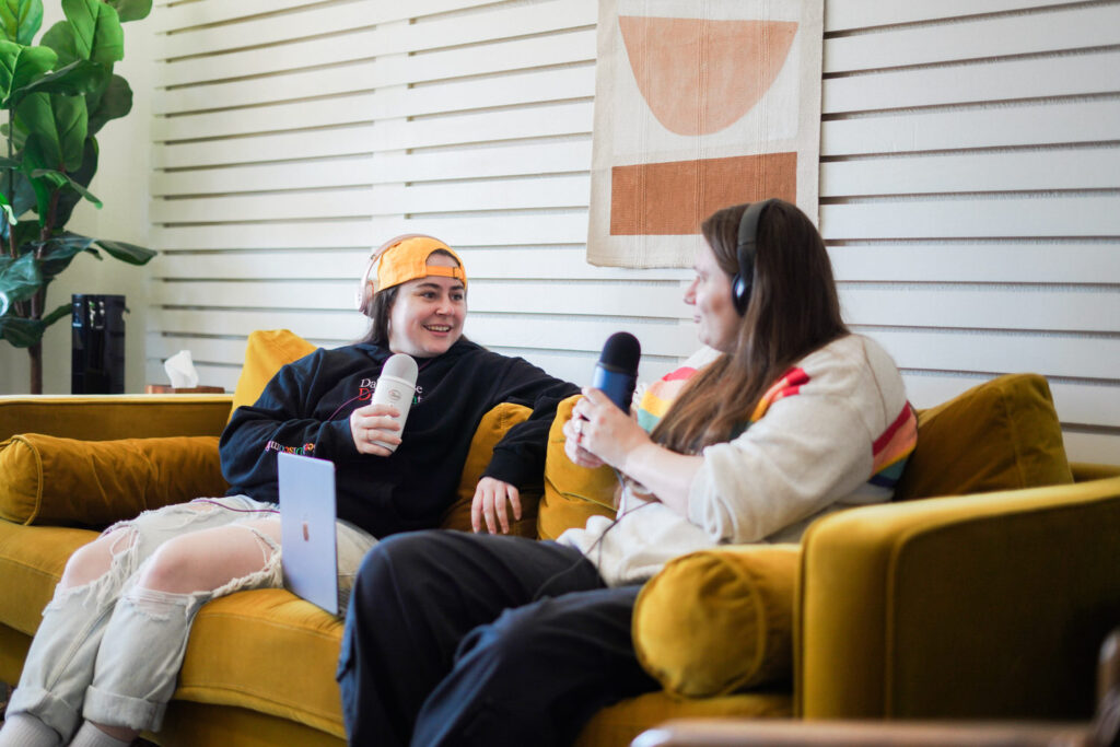 KP and Jessie talk while podcasting on a yellow couch.