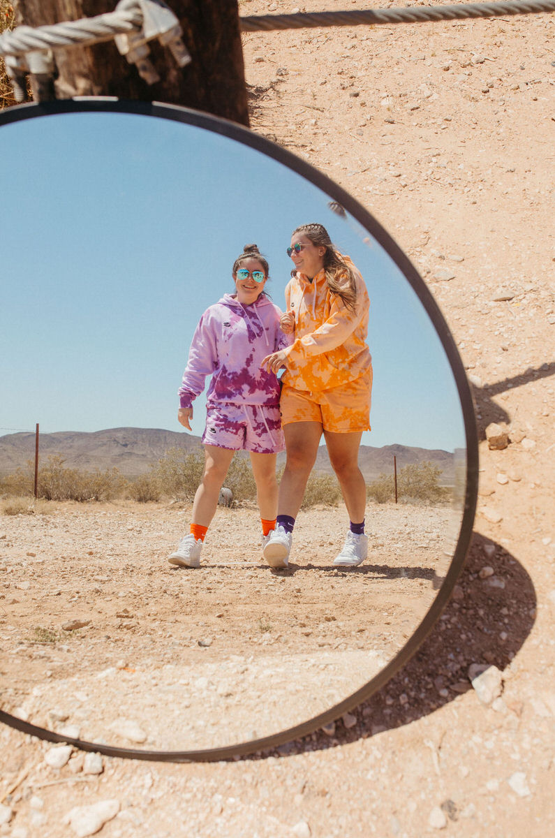 Reflection in a mirror of two people in color sweatsuits walking in the desert.