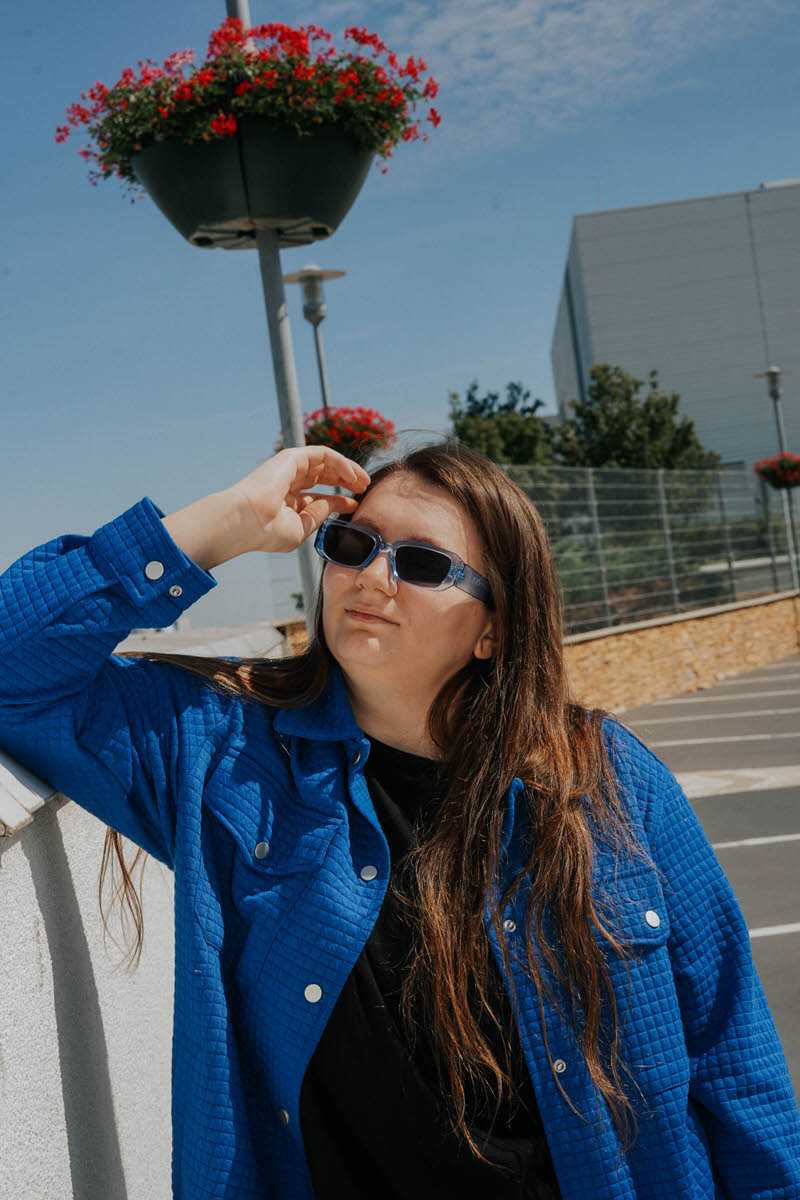 A woman leaning on a wall with one hand in her hair.