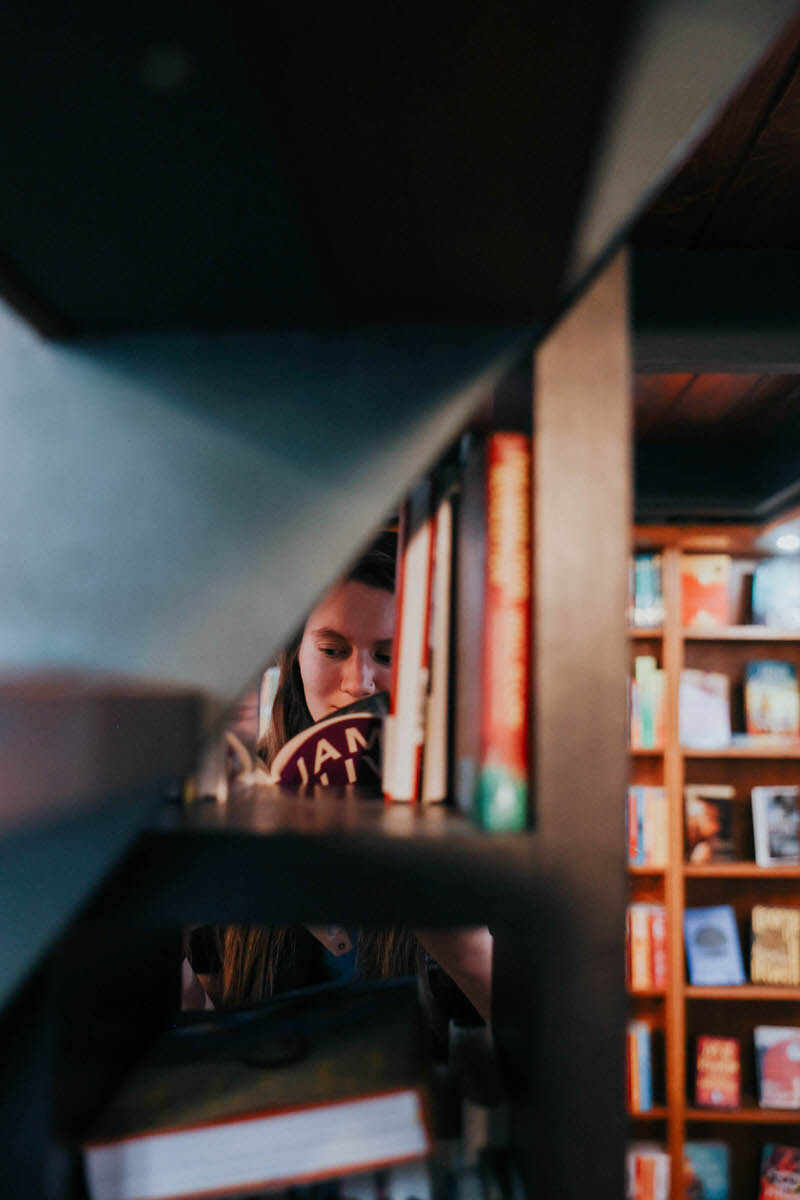 Image of a person reading a book seen through a hole in a bookcase.