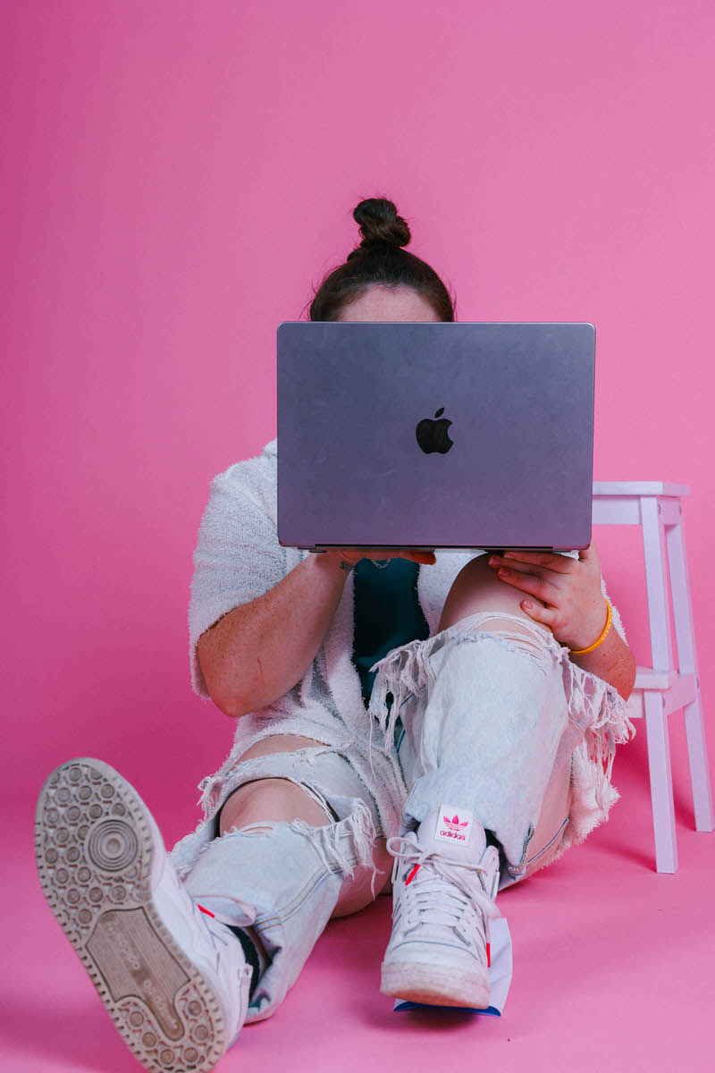 A woman sitting on the ground with a laptop balancing on her knee