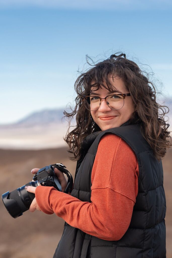 A person looking over their shoulder smiling and holding a camera.