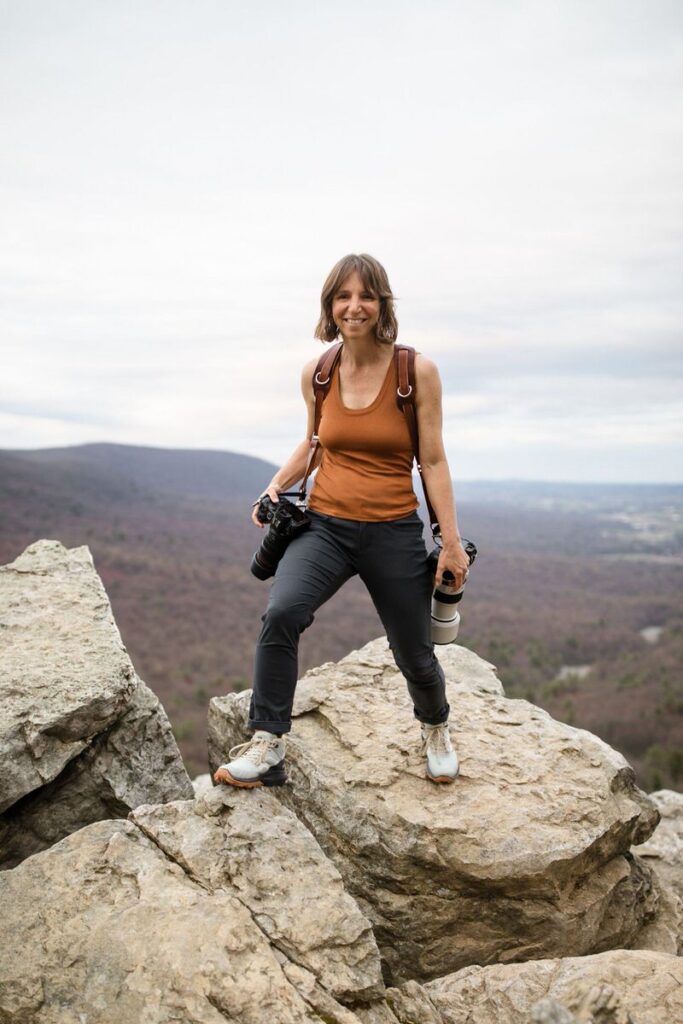 A photographer standing on rocks with two cameras smiling