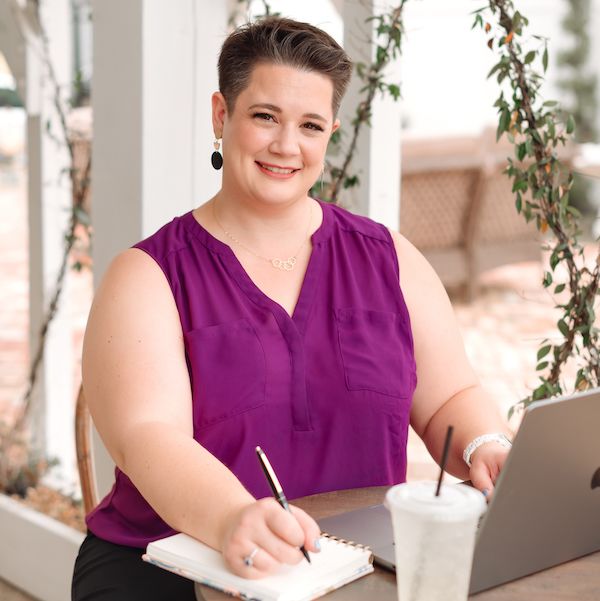 A woman writing in a notebook while smiling at a desk