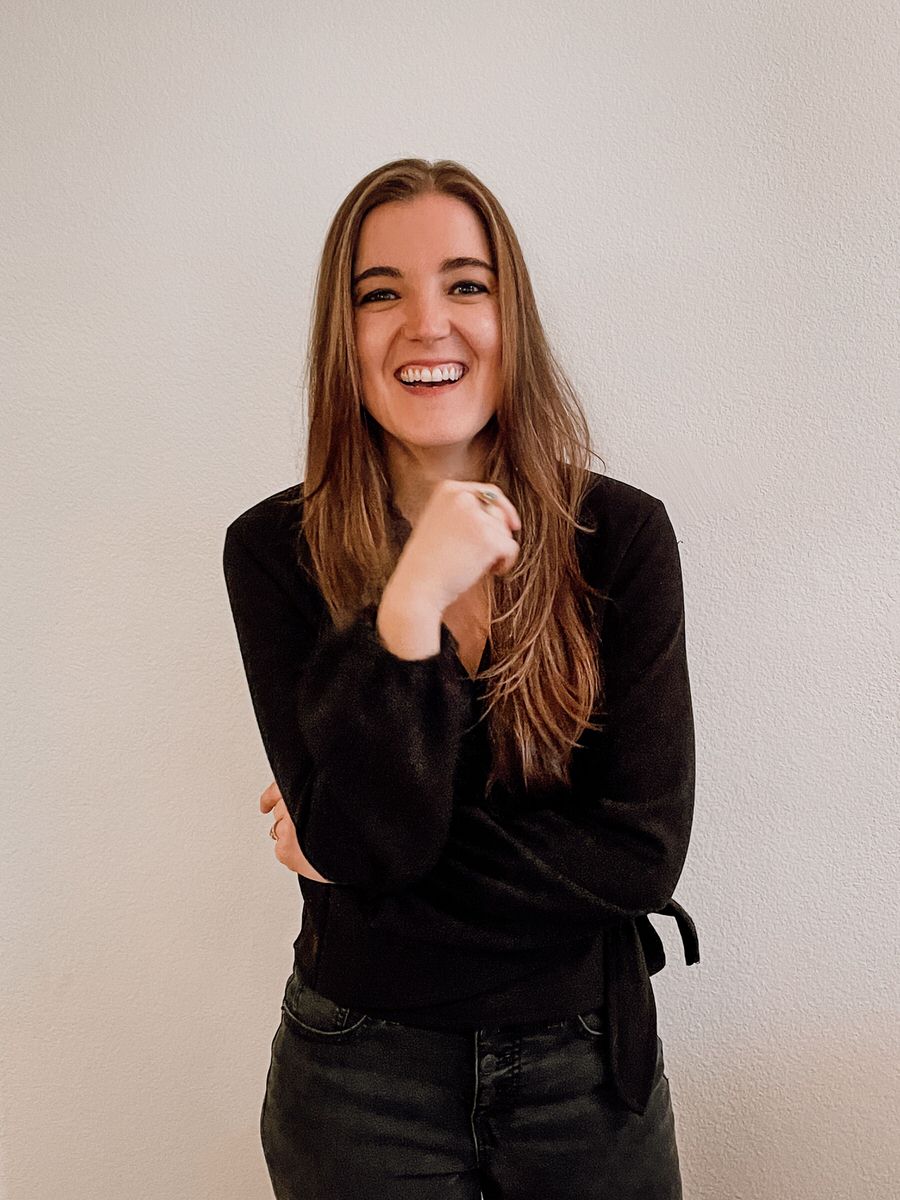 A person standing with one hand up towards her chin as she smiles