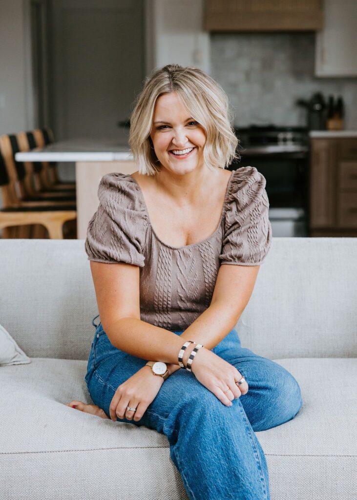 A woman sitting on a couch with a smile and her arms crossed on her legs. 