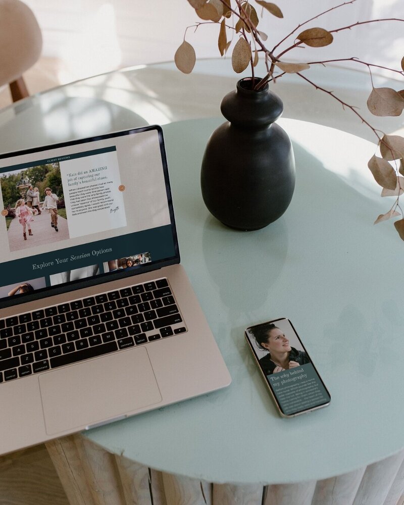 a laptop displaying the website for kate simpson photography on top of a table on the table there is also a phone dispalying the website for kate simpson photography