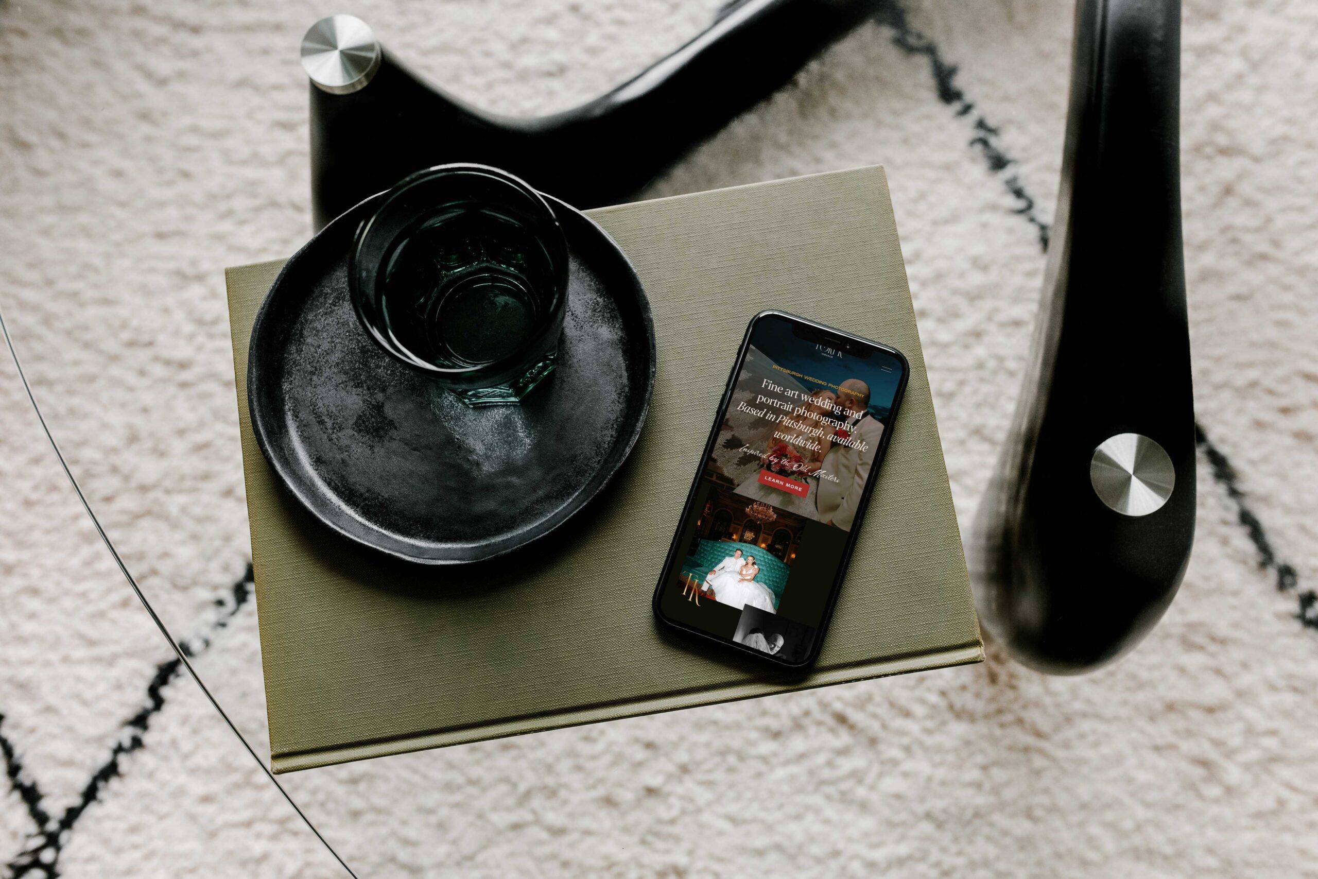 a phone on top of a green box on the phone is displayed the website for tori k visuals also on top of the green box in a black plate and mug